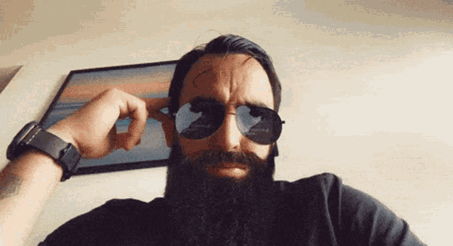 a man with a beard is wearing sunglasses and adjusting them