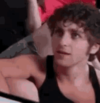 a man in a black tank top is sitting in a crowd of people .
