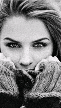 a black and white photo of a woman in a sweater covering her face with her hands .