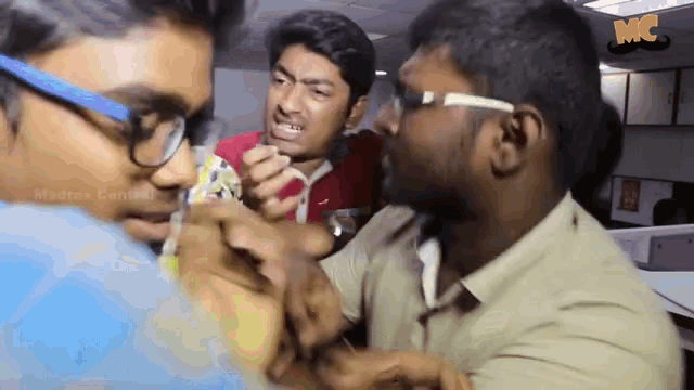 a man wearing glasses is holding another man 's hand in a room with a sign that says mc