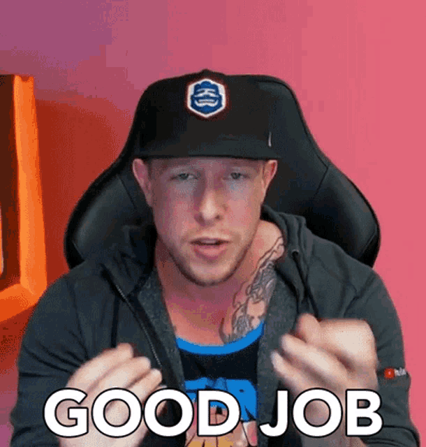 a man wearing a hat and a hoodie is sitting in a chair and giving a good job sign .