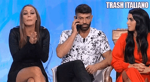 a man is sitting in a chair talking on a cell phone while two women applaud .