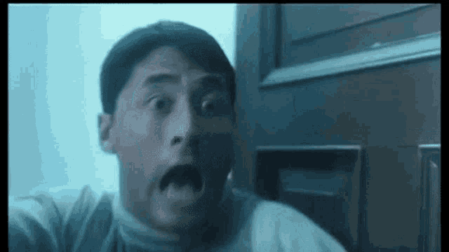 a man is making a surprised face while looking out a window .