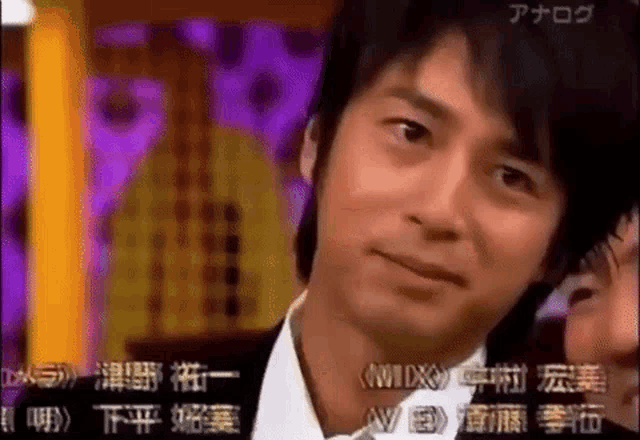 a man in a tuxedo is looking at the camera with a purple background behind him .