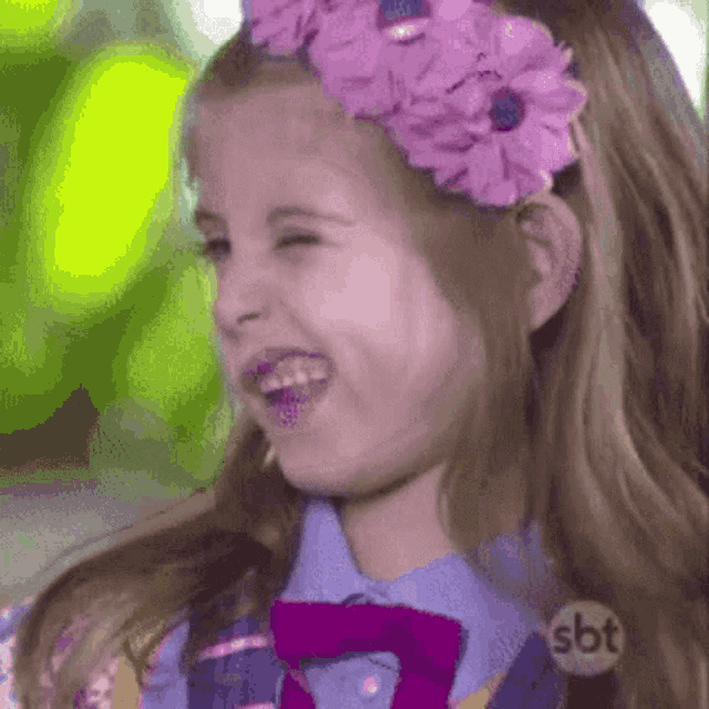a little girl wearing a purple headband and a purple bow tie is laughing .