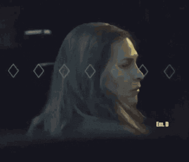 a close up of a woman 's face in a dark room with the words em.d. below her .