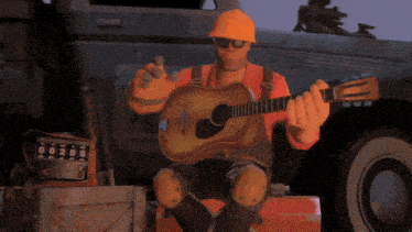 a man in an orange hard hat is playing an acoustic guitar in front of a truck