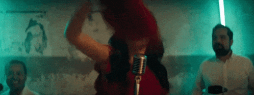 a woman in a red dress is singing into a microphone while a man watches .