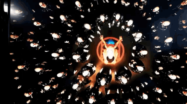 a group of people are dancing in a dark room with a circle of lights around them