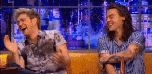 two men are laughing together while sitting next to each other on a couch .