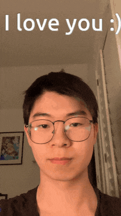 a young man wearing glasses takes a selfie with the words i love you behind him
