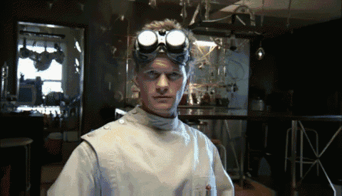 a man wearing goggles and a lab coat looks at the camera