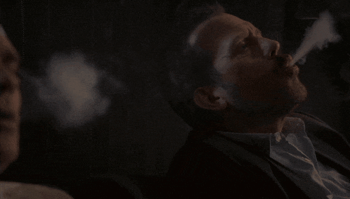 a man in a suit is smoking a cigarette with smoke coming out of his mouth