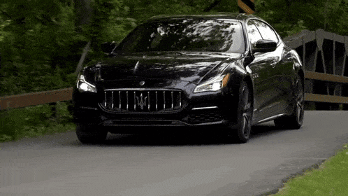 a black maserati is driving down a road next to trees .