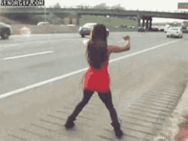 a woman in a red dress is standing on the side of a highway .