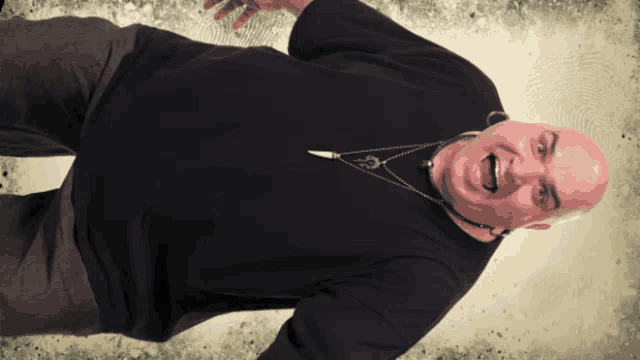 a bald man wearing a black shirt and a necklace with a bullet pendant on it
