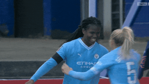 two female soccer players wearing etihad airways jerseys are hugging