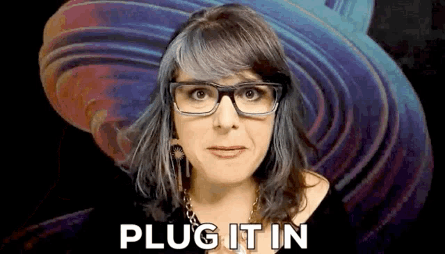 a woman wearing glasses and earrings says plug it in .