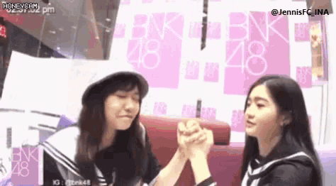 two young women are holding hands in front of a pink wall .