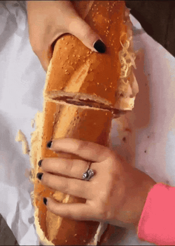 a woman with a ring on her finger is holding a large sandwich