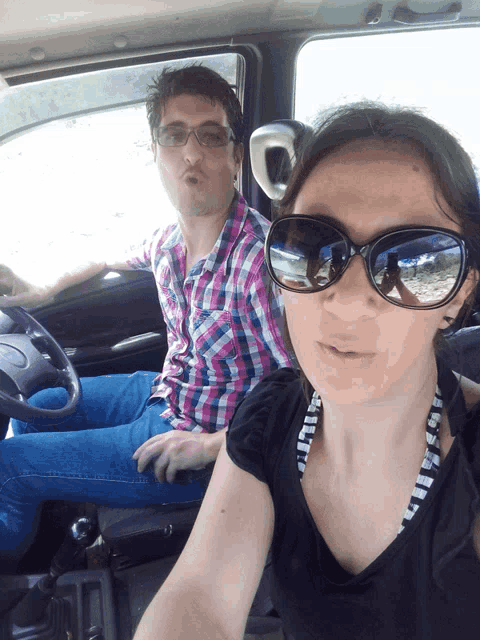 a man and a woman are sitting in a car and the woman is wearing sunglasses