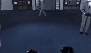 a group of people are standing in a room in a video game and a man is standing in the middle of the room .