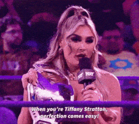 a woman is holding a trophy and speaking into a microphone while standing in a wrestling ring .