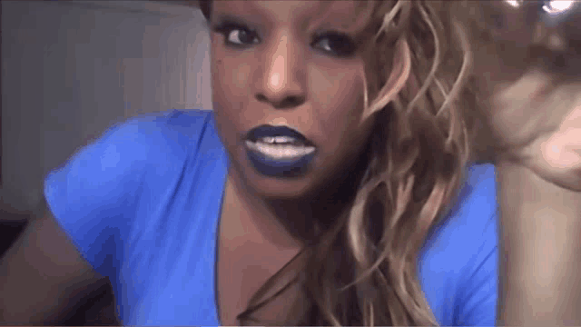 a woman wearing blue lipstick and a blue shirt looks at the camera