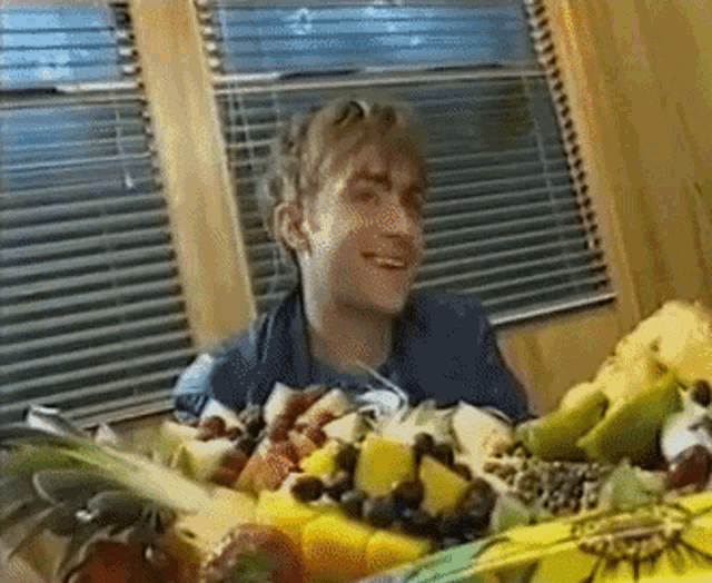 a man is sitting in front of a bowl of fruit and smiling