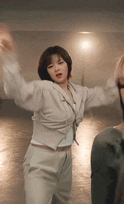 a woman in a white jacket and white pants is dancing in a dark room
