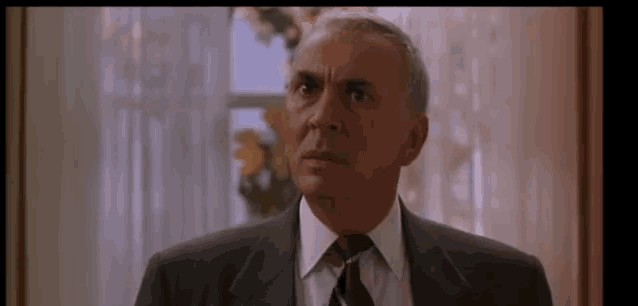 a man in a suit and tie is looking at the camera with a surprised look on his face .
