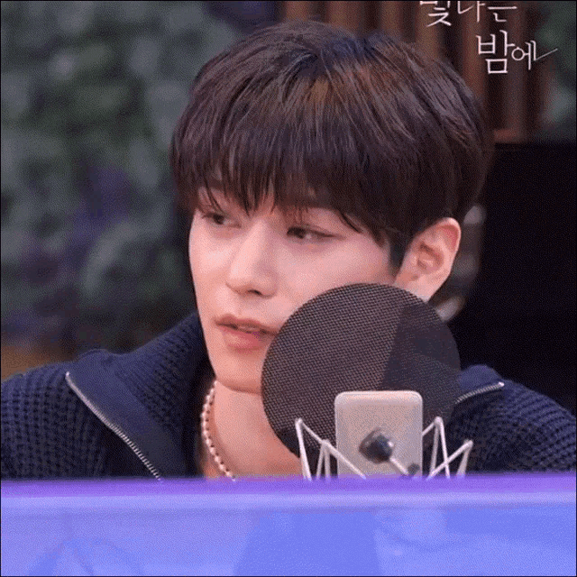 a young man sitting in front of a microphone with korean writing on the bottom right