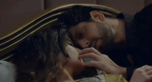 a man and woman are kissing on a bed and the man is touching the woman 's face