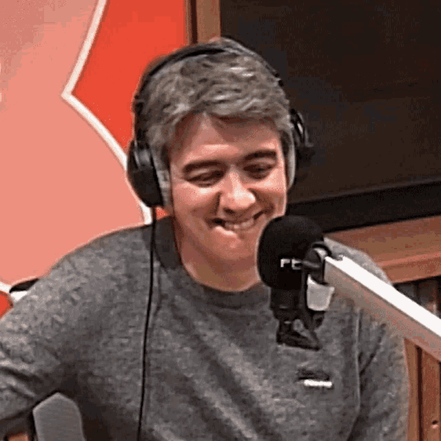 a man wearing headphones is smiling in front of a microphone with the letter f on it