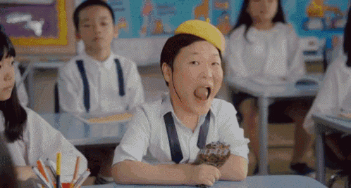 a group of children are sitting at desks in a classroom with a boy wearing a yellow hat .