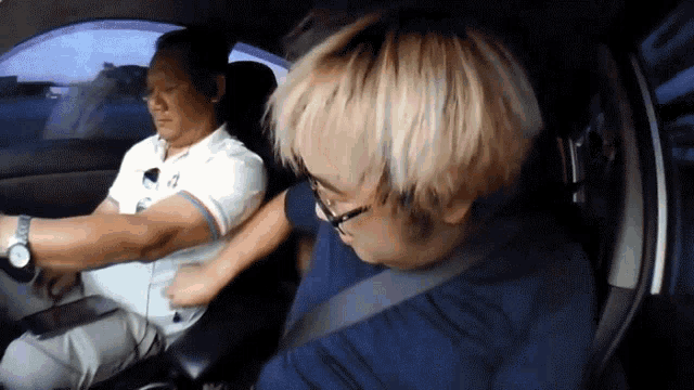a man wearing a watch is driving a car with another man sitting in the back seat