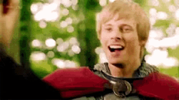 a man in a red cape is smiling and talking to another man in a forest .