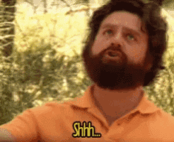 a man with a beard is wearing an orange shirt and says shhh