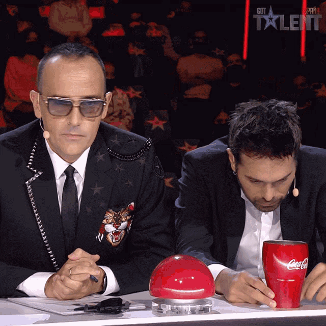 two men are sitting in front of a red coca cola cup
