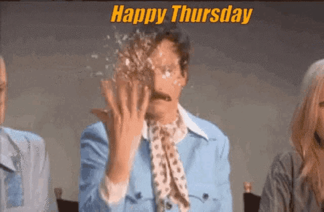 a man with a mustache is sitting in front of a group of people with a happy thursday greeting .