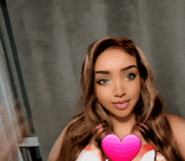 a woman with long hair is holding a pink heart in her hands .