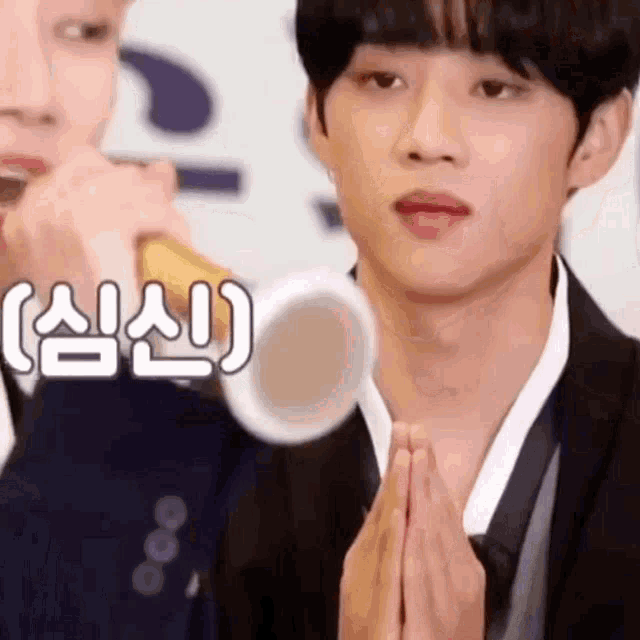 a man in a suit and tie is praying with his hands folded in front of a microphone .
