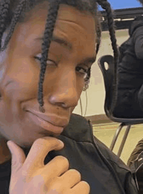 a man with braids is making a funny face while sitting at a desk in a classroom .