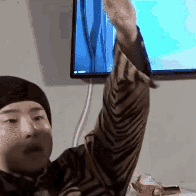 a man is sitting in front of a television with his arm up .