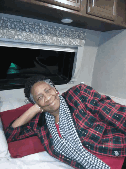 a woman in a plaid jacket is laying on a bed with her head on a pillow
