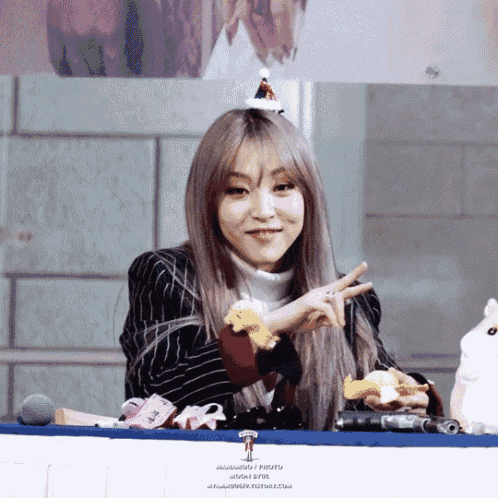 a woman wearing a striped jacket and a turtleneck is giving the peace sign