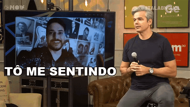 a man holding a microphone stands in front of a tv screen that says to me sentindo