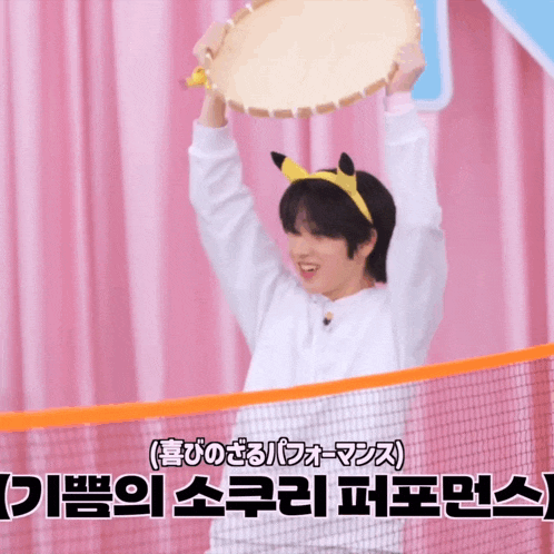 a boy wearing a pikachu headband holds up a drum