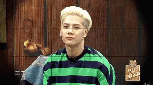 a young man with blonde hair is wearing a green and blue striped shirt and looking at the camera .