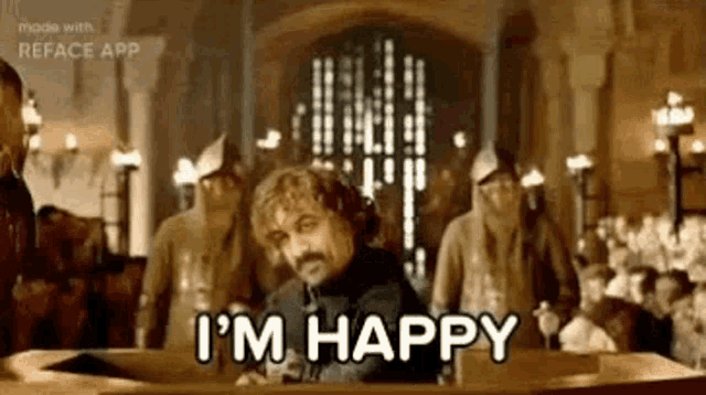 a man with a mustache is sitting in a chair and saying `` i 'm happy '' in front of a crowd .